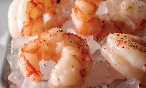Close-up of four cooked shrimp sitting on ice.