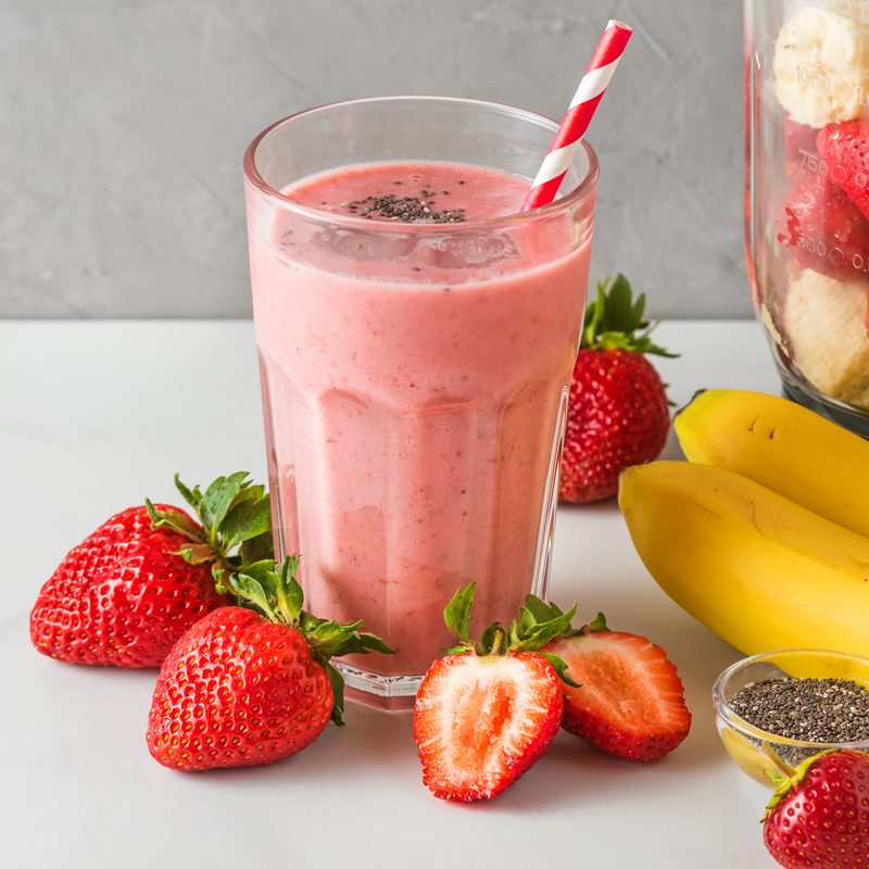 A glass of strawberry smoothie, surrounded by strawberries and bananas.