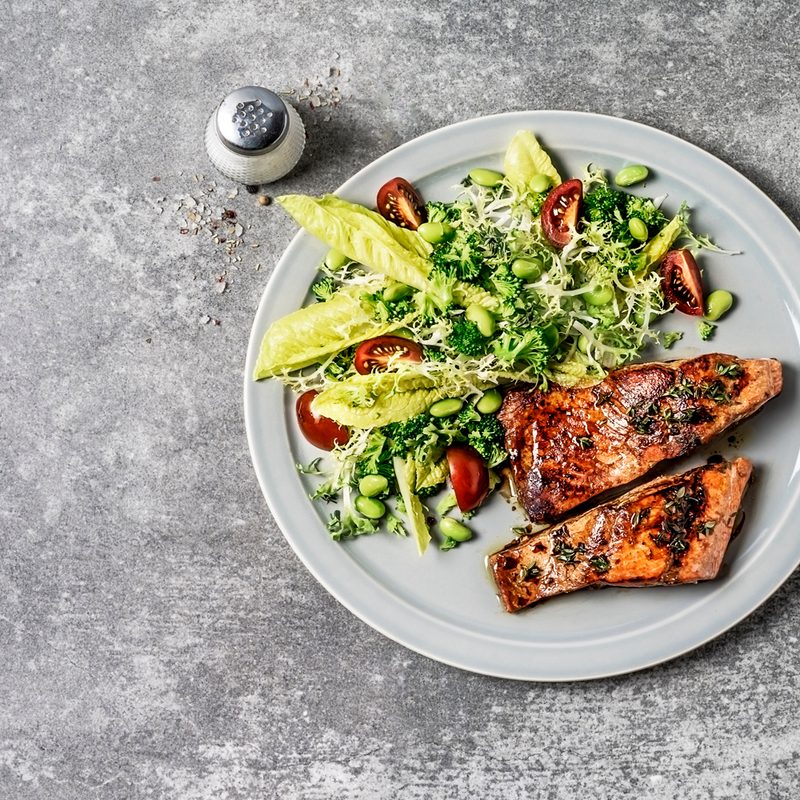 Salmon with greens served on a plate on a gray table.