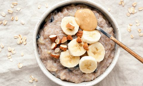 A spoonful of peanut butter and a bowl of oatmeal with banana slices.