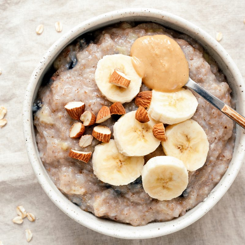 A spoonful of peanut butter and a bowl of oatmeal with banana slices.