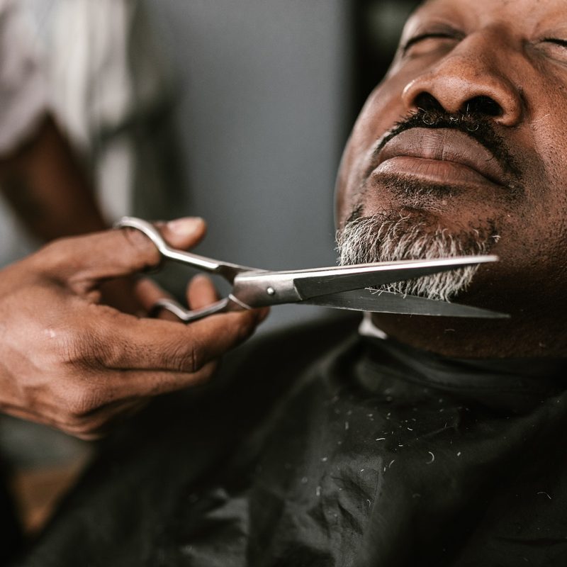 barber trimming man's goatee with scissors.