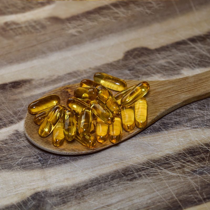 Spoonful of cod liver oil supplements on wooden background