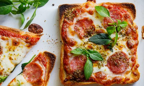 Pizza toast with ham and cheese garnished with herbs.