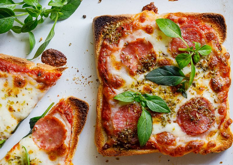 Pizza toast with ham and cheese garnished with herbs.