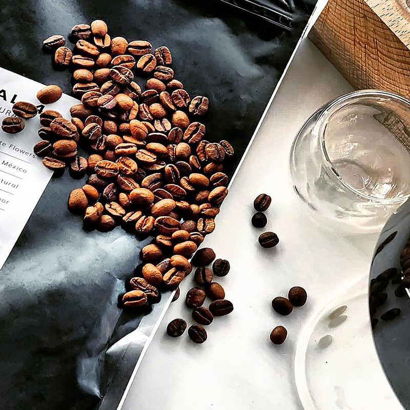 Coffee beans on an empty Quintal Coffee pack beside a brewer and an empty cup.