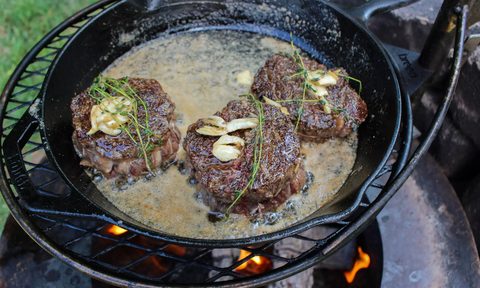 Ribeye caps topped with garlic and herbs cooked in a cast iron pan over charcoal.