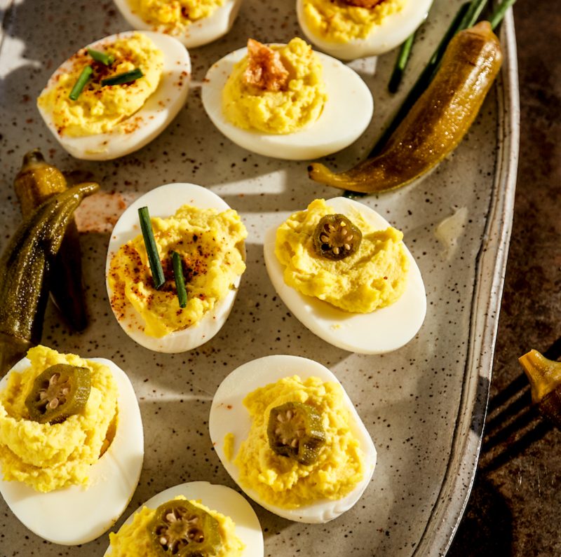 Rodney Scott deviled eggs with pickled okra on a metal tray with a red fork.