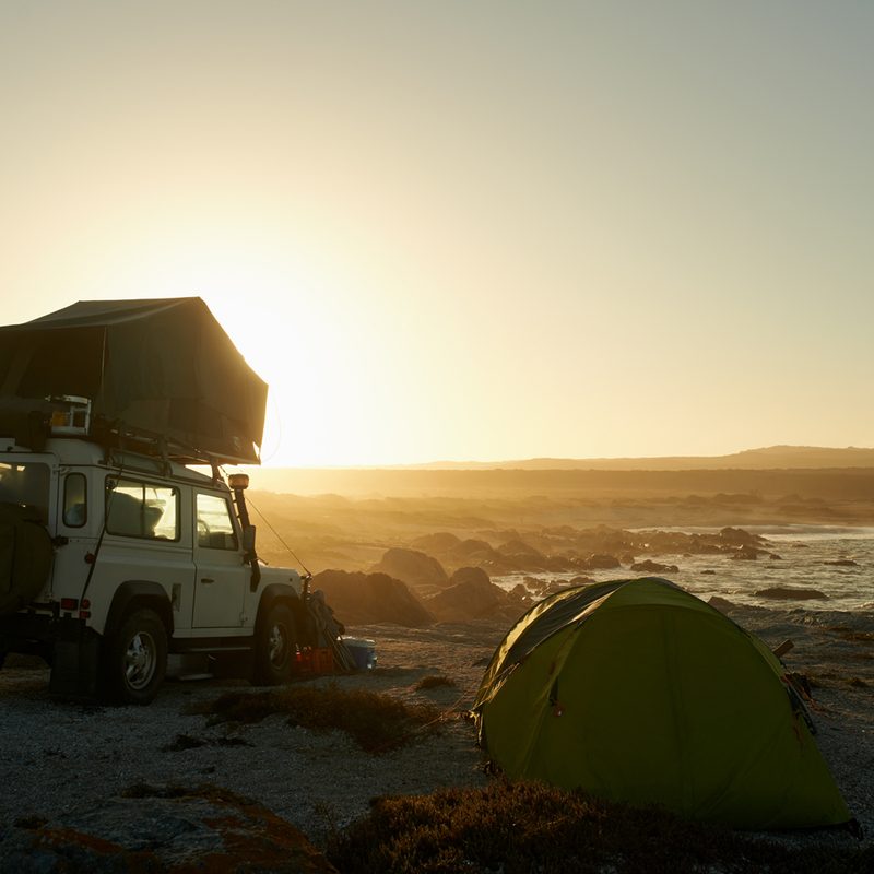 A silhouette of a man and a vehicle with a rooftop tent in the wilderness.