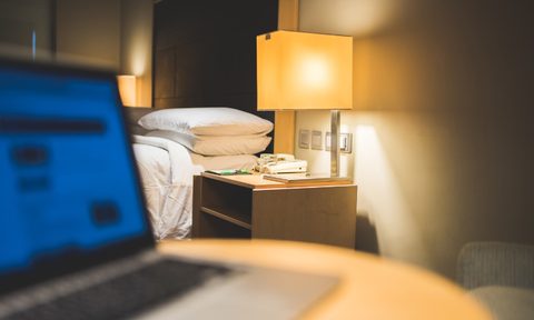 Hotel Room with a Notebook Computer on the Table Near the Bed