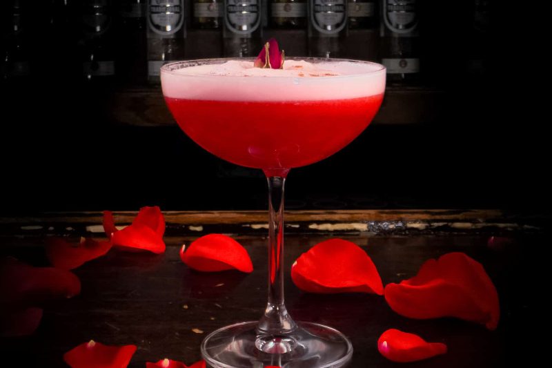 A margarita in a glass surrounded by rose petals.