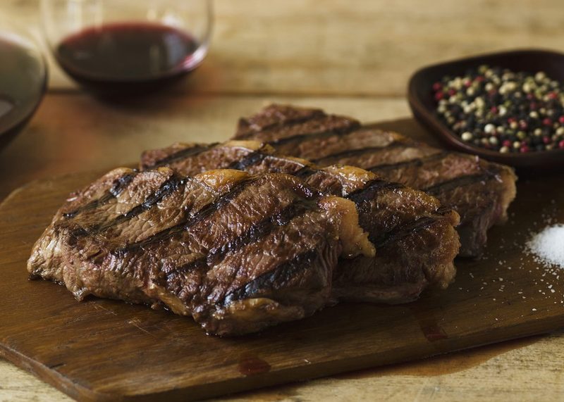 Slices of steak, a bowl of peppercorn, and salt mound on a wooden cutting board