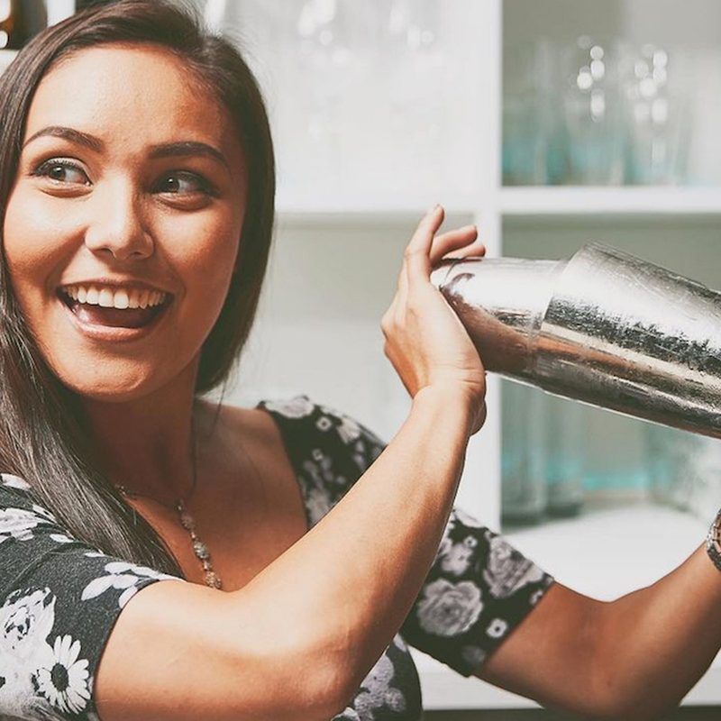 Kira Webster smiling and shaking a cocktail.