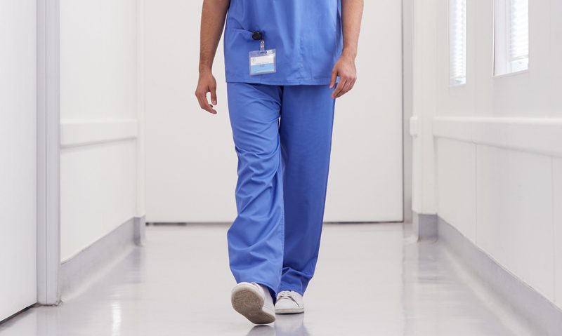Young,Male,Doctor,Wearing,Scrubs,Walking,Along,Hospital,Corridor