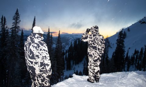 Two people wearing a matching winter coats and snow pants from The North Face XX Kaws collection.