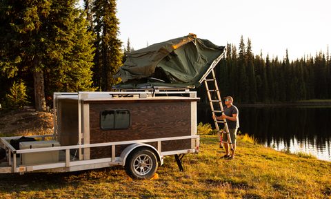 A man climbing a ladder to set up a rooftop tent on top of his vehicle in the campsite.