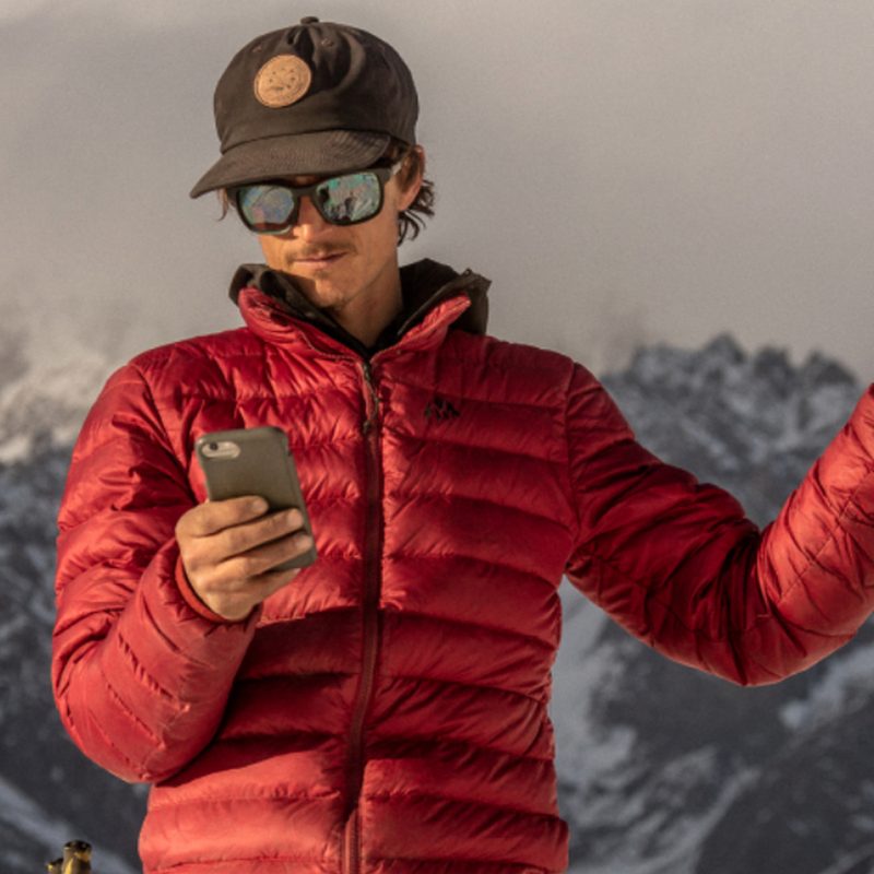 A man holding a phone in his right hand and a Somewear Global Hotspot in his left hand on a mountain.