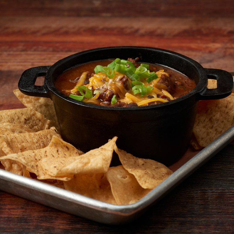 Virgil's chili in a black bowl surrounded by tortilla chips.