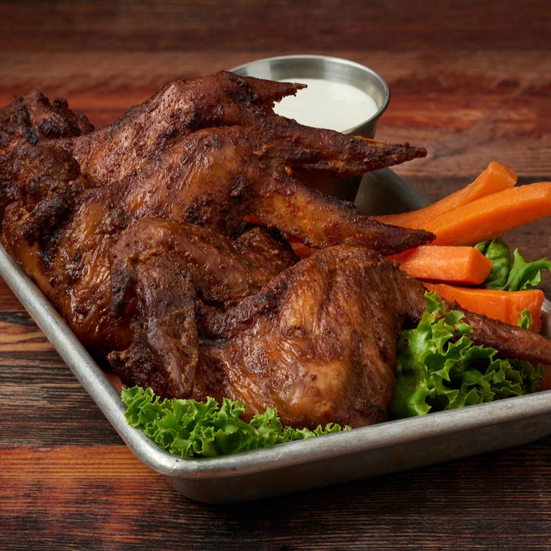 Virgil's smoked wings on a metal tray with raw carrots placed on a wooden table.