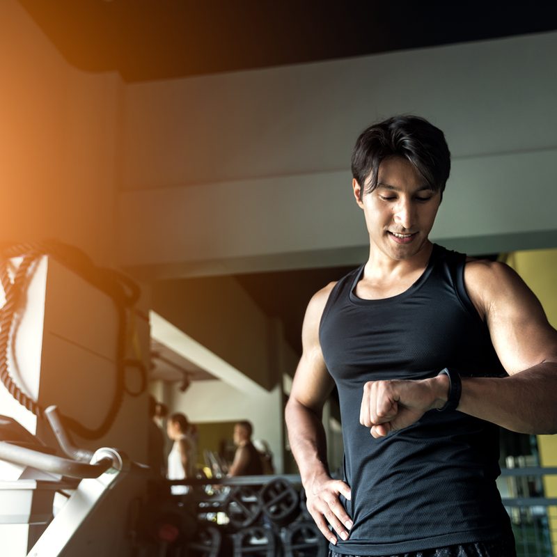 A male athlete looking at his watch in a gym.