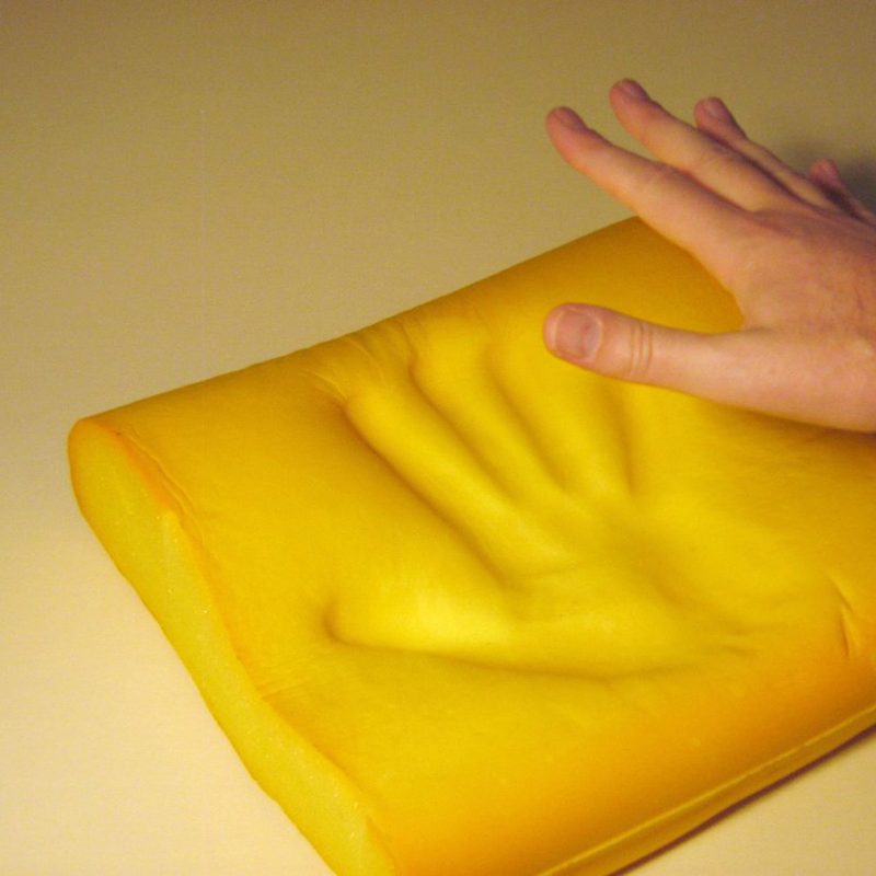 A person's hand and a memory foam pillow material with handprint.