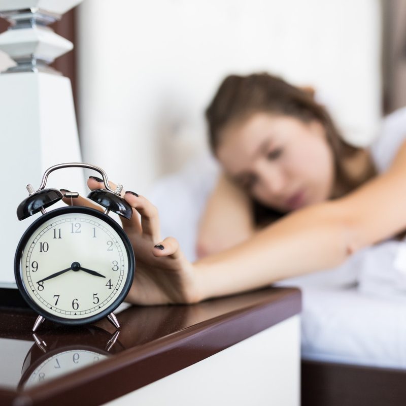 A woman reaches an alarm clock from her bed.