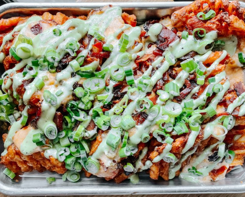 A tray of Emmy Squared waffles fries covered in toppings on a metal tray.