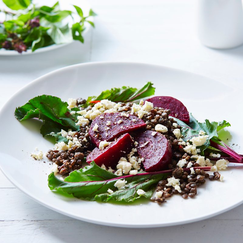 Two plates of beetroot and feta salad beside two cups on white table.