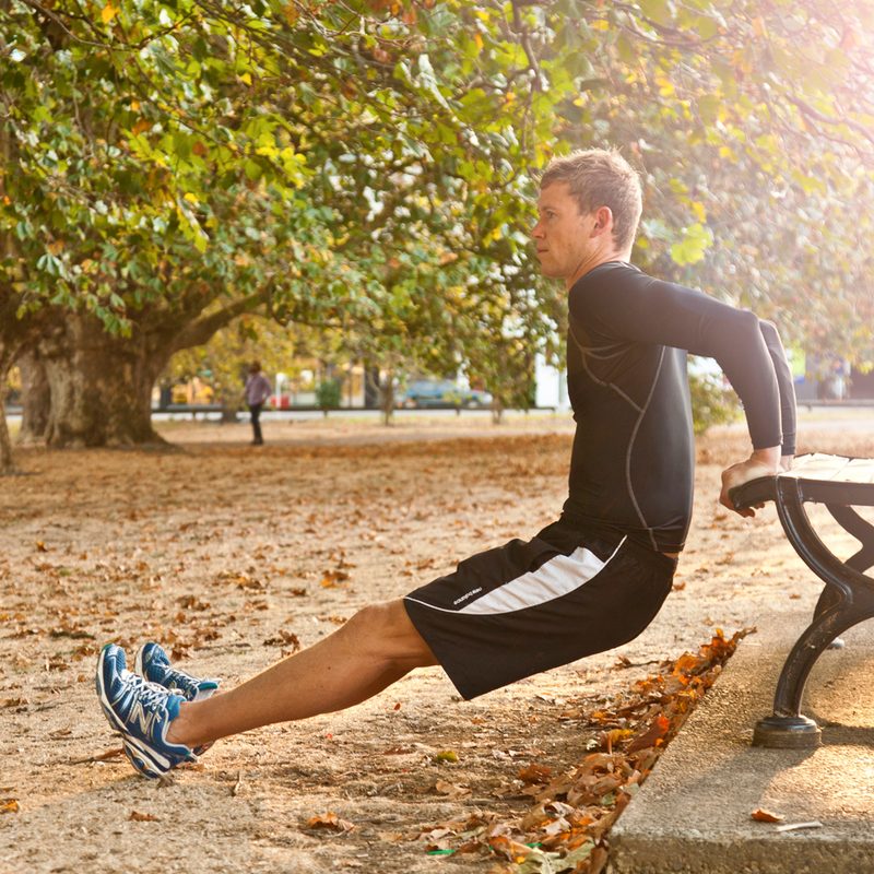 A man doing dips using a bench at a park.