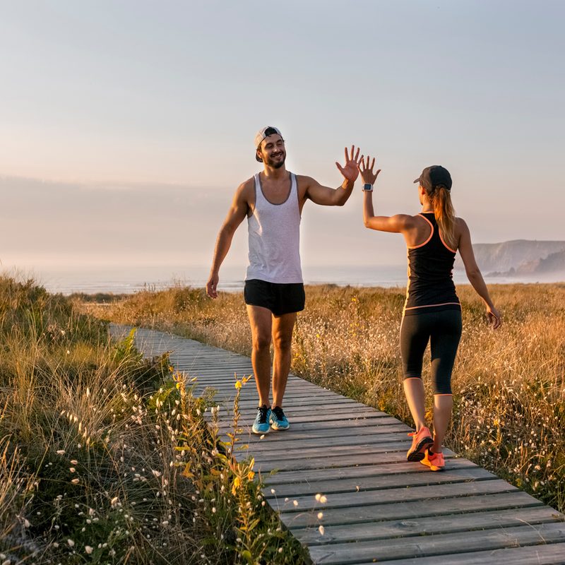 A man and a woman in sportswear doing a high five on a wooden walkway on a grassy field.