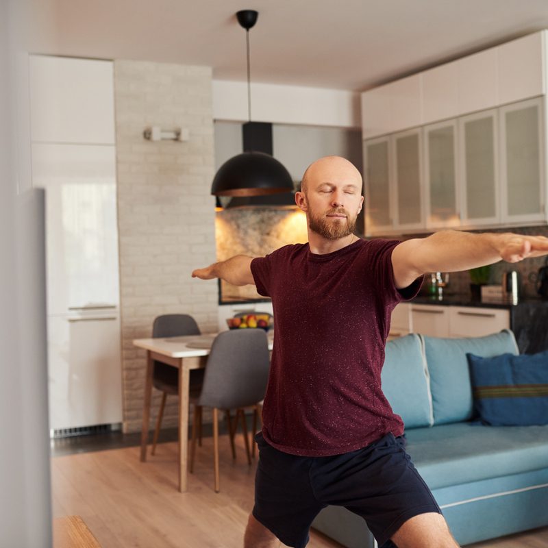 A man doing a warrior pose with his eyes closed in the living room.