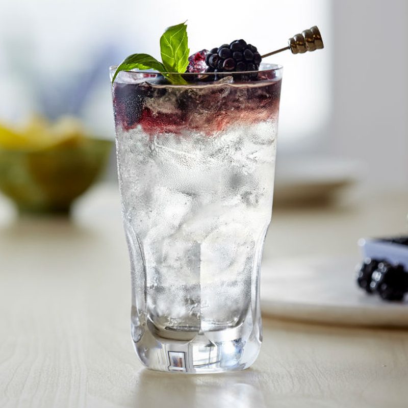 A Bacardi Blackberry Bramble garnished with basil and blackberry skewer with a tray of blueberries in the background.