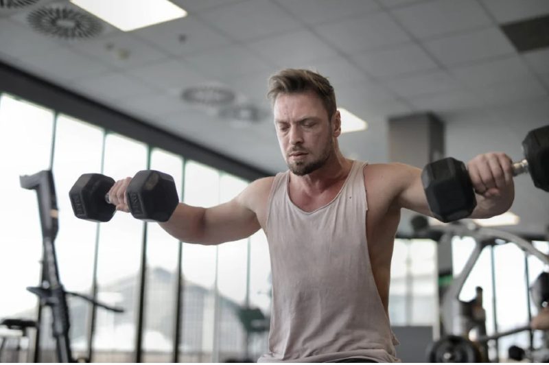 Guy in a gym performs a dumbbell lateral raise.
