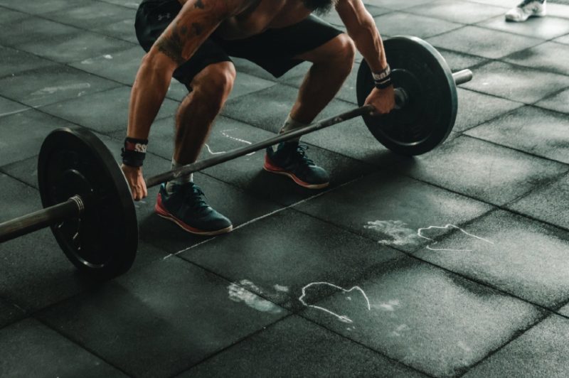 Guy at a gym grabs a barbell to start a snatch exercise.