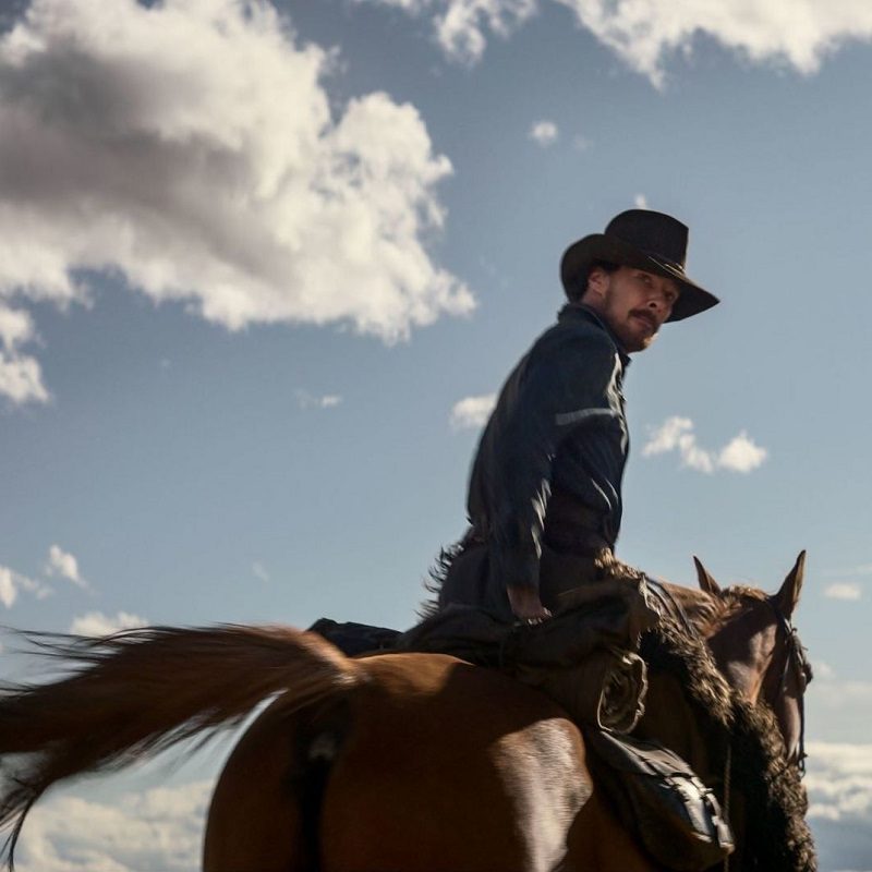 Benedict Cumberbatch looking back as he rides a horse in The Power of the Dog.