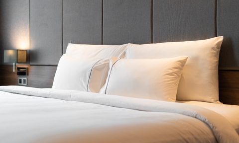Four white pillows propped up on a bed in a room.