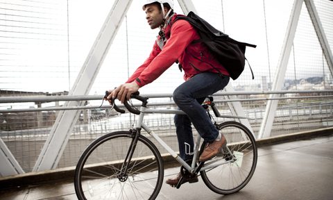 A man with black backpack and white helmet cycling to work on a road.