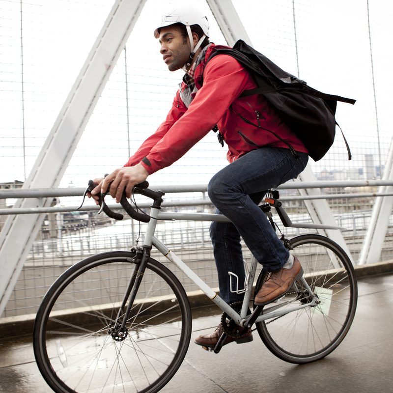 A man with black backpack and white helmet cycling to work on a road.