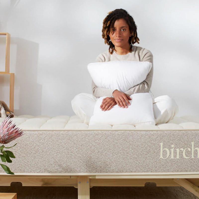 A woman and her dog sit on top of a Birch by Helix Natural mattress.