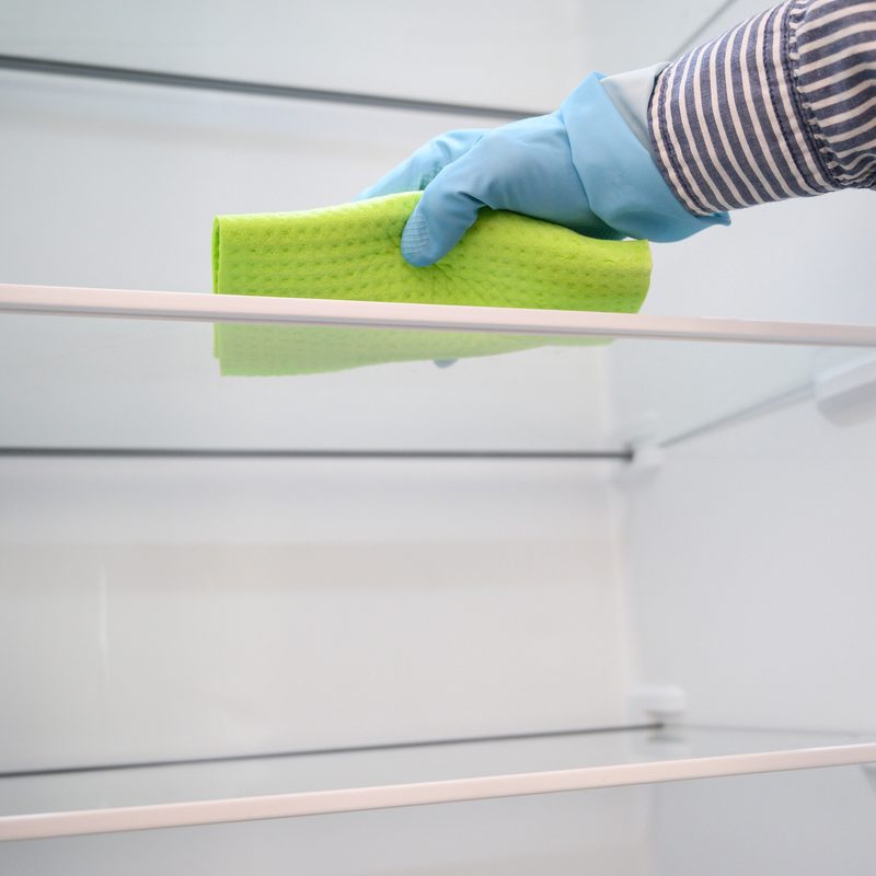 Person with protective plastic gloves cleaning inside the fridge with a ballot.
