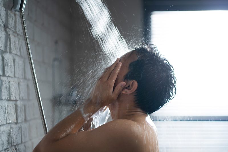 A side profile of a man washing his face in the shower.