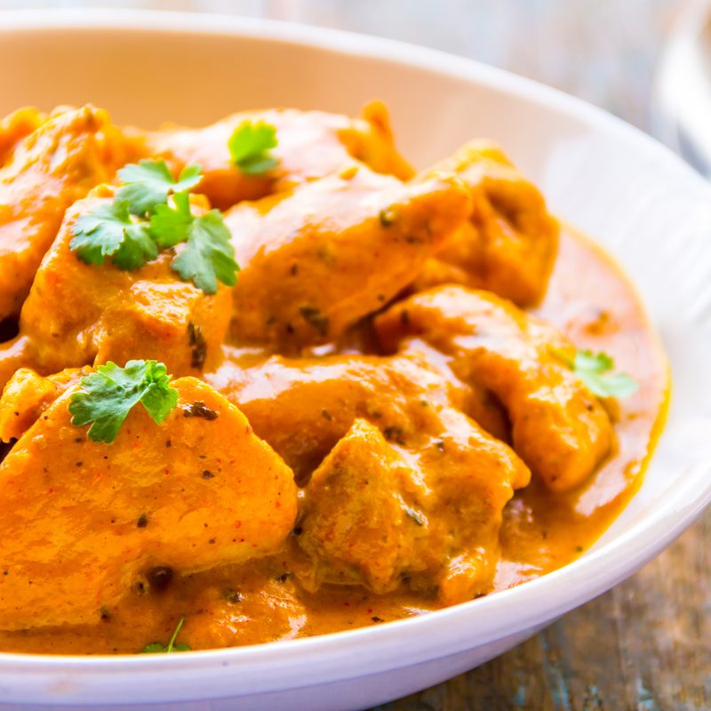 A close-up of a butter chicken served on a bowl with spoon on a table.