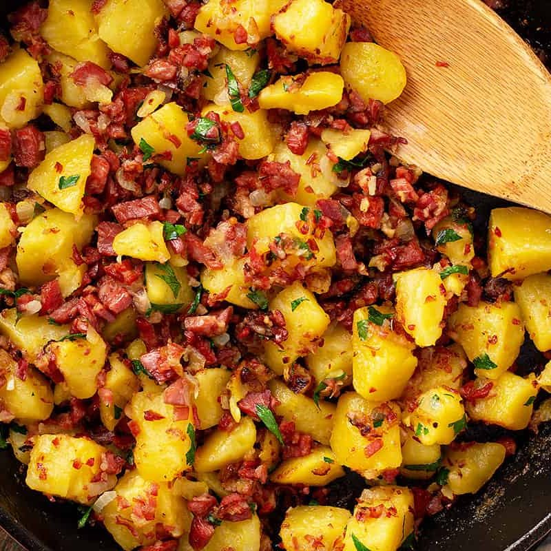 Corned beef hash in a cast iron with wooden spoon.