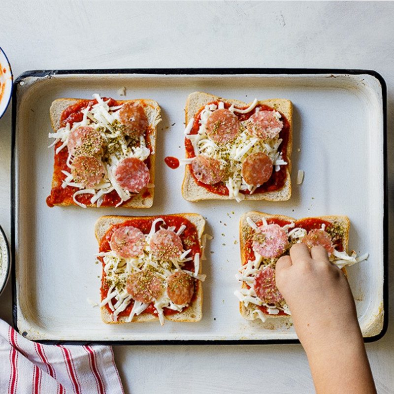 person making pizza toast on a sheet tray.