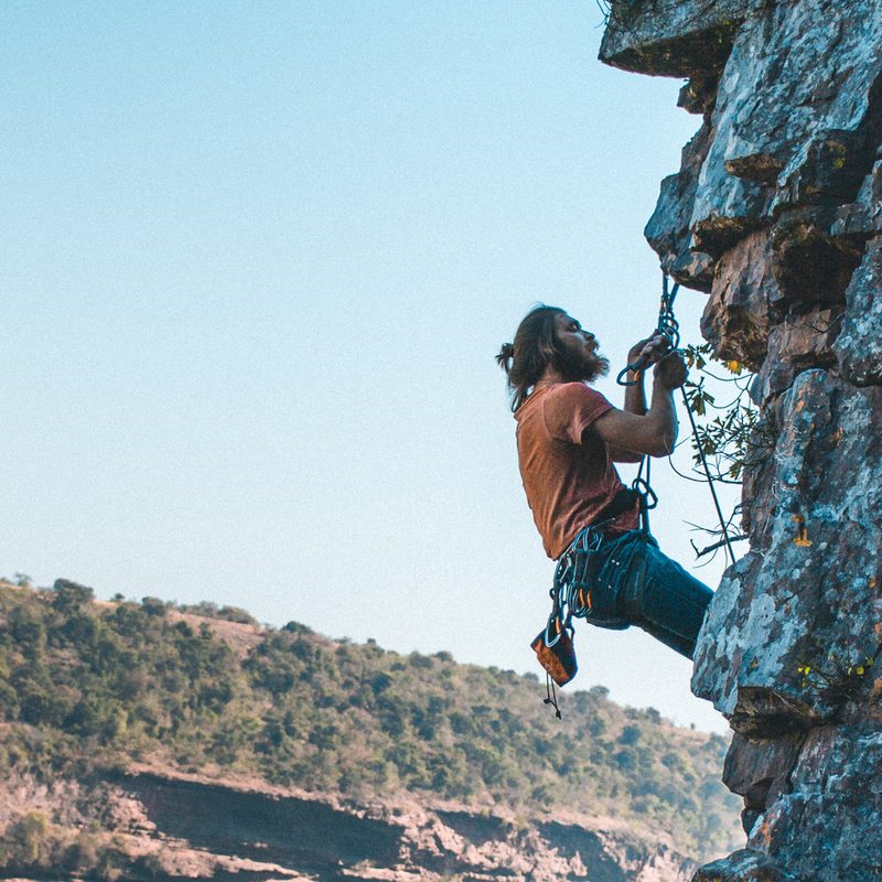 A man in orange t-shirt free climbing a rock formation in the morning.