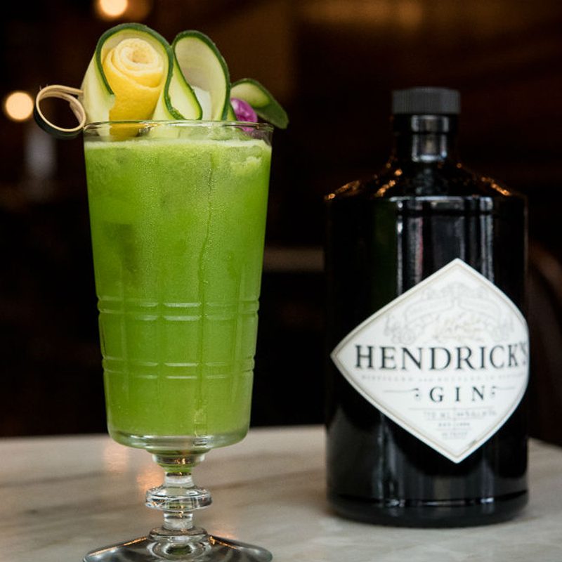 A refreshing glass of Fresh Perspective garnished with vegetables beside a bottle of Hendrick's Gin.
