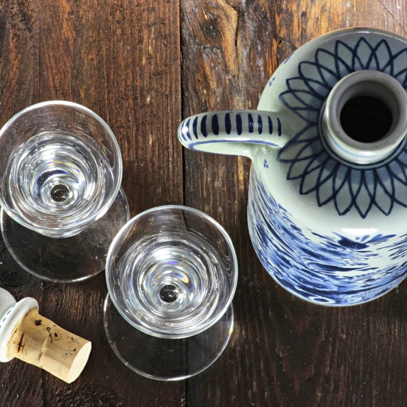 An overhead shot of two glasses of genever beside an opened bottle with handle and its cork on wooden table. 