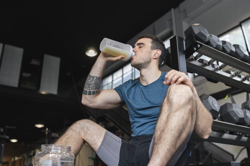 Male athlete drinking protein shake while sitting in gym.