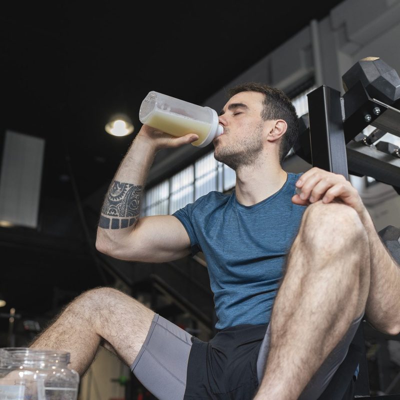 Male athlete drinking protein shake while sitting in gym.