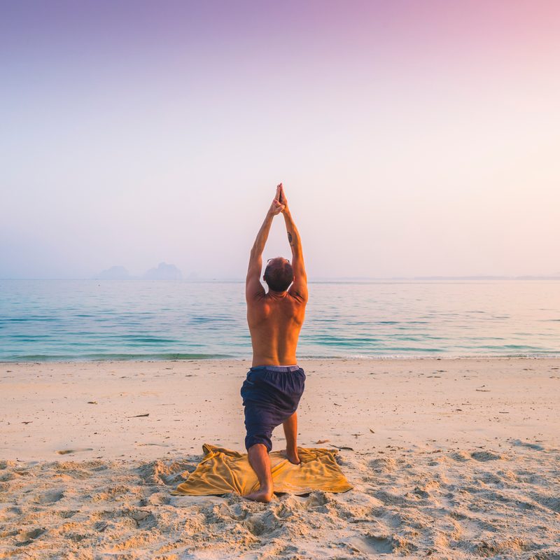 Man practicing yoga on the beach.